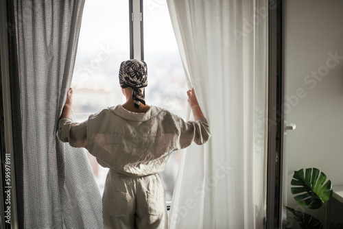 Rear view of young unhappy woman with cancer standing in front of a window. © Halfpoint