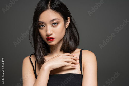 portrait of elegant asian woman with red lips looking at camera isolated on grey.