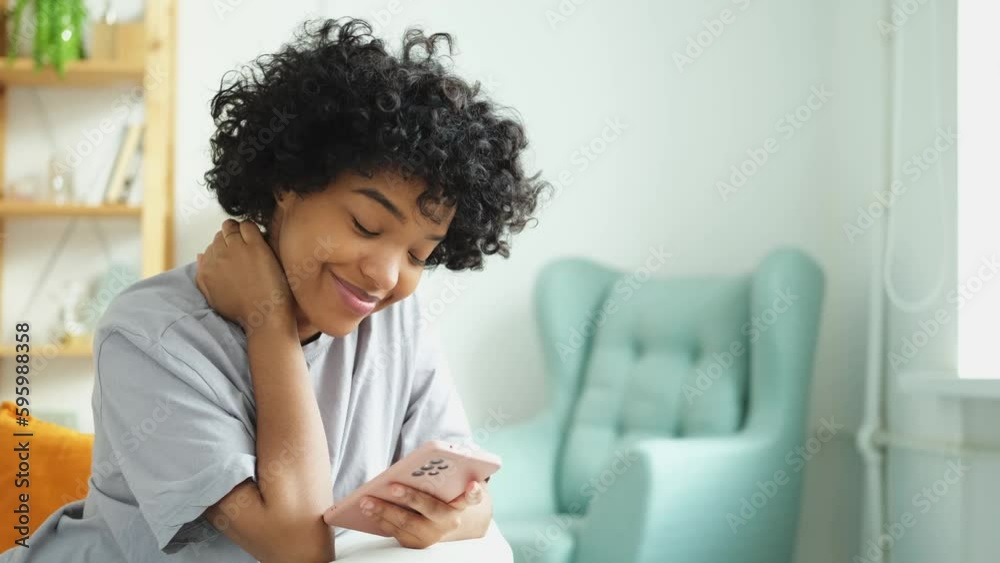 African girl holding smartphone touch screen typing scroll page at home. Woman with cell phone surfing internet using social media apps playing game. Shopping online Internet news cellphone addiction African girl holding smartphone touch screen typing scroll page at home. Woman with cell phone surfing internet using social media apps playing game. Shopping online Internet news cellphone addiction