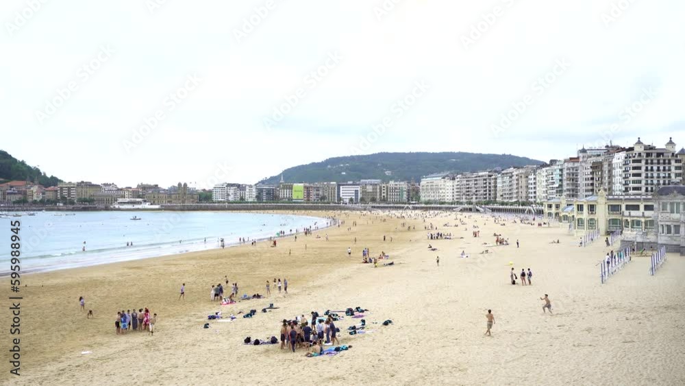 San Sebastian, SPAIN - July 09 2022. Panoramic view of beautiful city San Sebastian - Donostia. View of La Concha Beach. People at the beach. Cloudy day. Stabilized static video. San Sebastian, SPAIN - July 09 2022. Panoramic view of beautiful city San Sebastian - Donostia. View of La Concha Beach. People at the beach. Cloudy day. Stabilized static video.