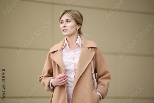 Portrait of a smiling young business woman in a coat straightening her coat with her hand, outside. Management concept