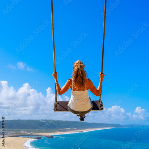 Woman sitting on swing flying in blue sky with view of sea or ocean- vacation,travel, tourism, freedom, relaxing concept