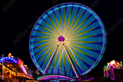 Ferris wheel on a german funfair “Kirmes“ or „Jahrmarkt“ at dark night with many colorful lights. Long time exposure that effects multi color light traces and abstract paintings isolated on black.