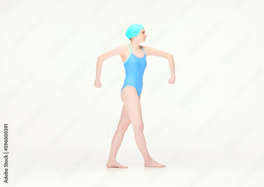 Young girl in blue swimsuit and swimming cap standing in position with broad hands isolated over white background. Concept of retro style, sport, fashion, youth, vintage. Copy space for ad Young girl in blue swimsuit and swimming cap standing in position with broad hands isolated over white background. Concept of retro style, sport, fashion, youth, vintage. Copy space for ad