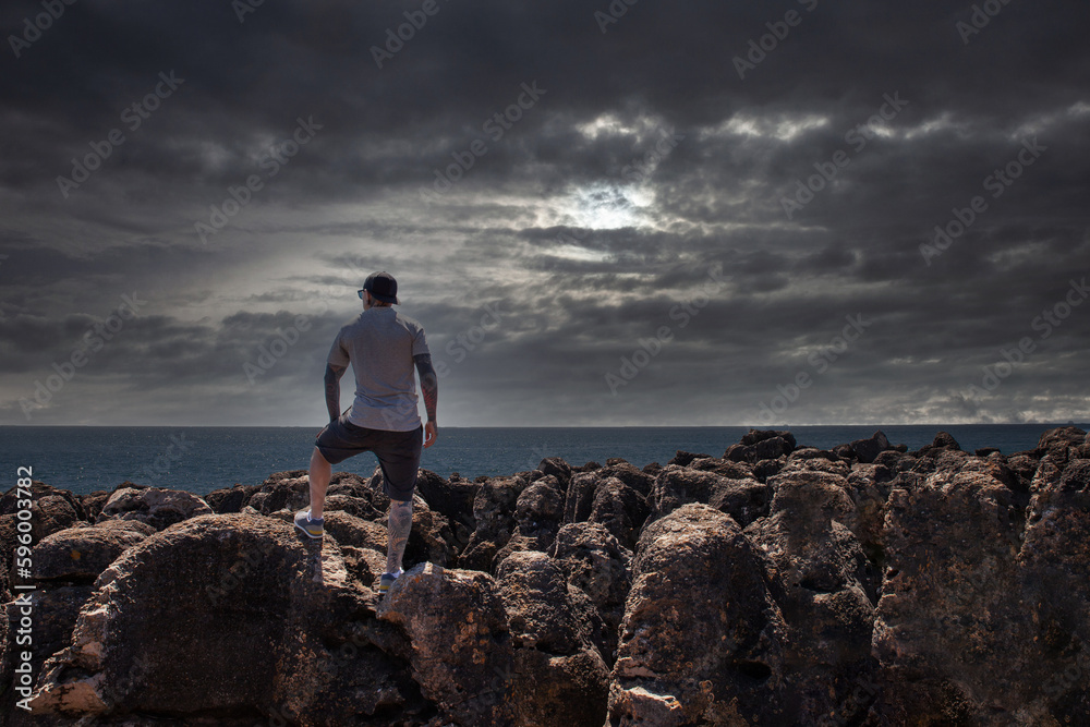 A man standing on the rocks and looking at the ocean. Dramatic sky, breathtaking view