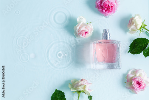 Perfume fragrance bottle on floral background. Top view of Transparent glass pink perfume bottle over rippled blue water background. splash of water. Flat lay, copy space