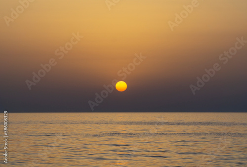yellow rounded sun and Beautiful yellow and violet dusk with calm ocean horizon line and no clouds sky