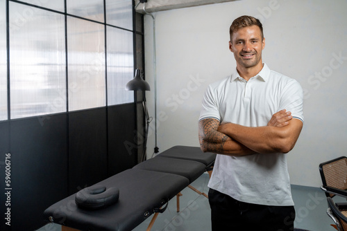 Cheerful masseur standing near massage table photo