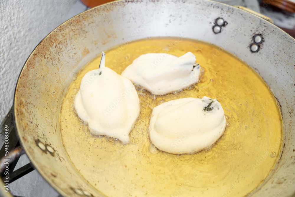 Three stuffed and battered poblano chilli peppers are being fried in a big metallic pan Three stuffed and battered poblano chilli peppers are being fried in a big metallic pan