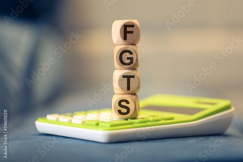 A sigla FGTS escrita em dados de madeira que estão sobre uma calculadora verde. Fundo de Garantia do Tempo de Serviço. Brasil. photo
