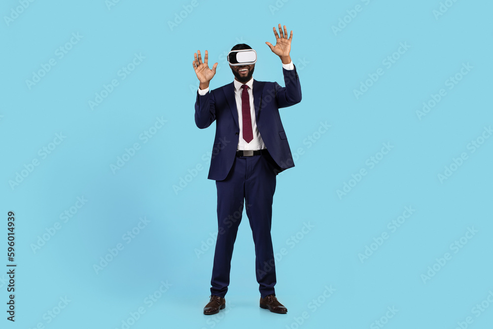 Excited Black Businessman In VR Headset Having Fun Over Blue Studio Background Excited Black Businessman In VR Headset Having Fun Over Blue Studio Background