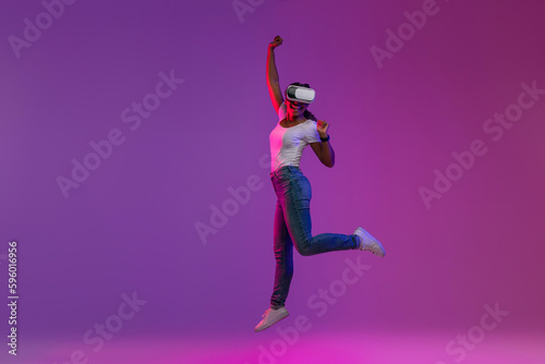 Carefree Black Female Wearing VR Headset Jumping Up In Neon Light