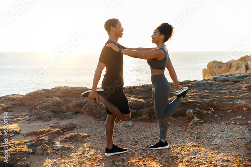Positive millennial african american couple in sportswear doing stretching for legs, practice yoga