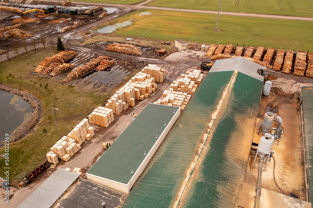 Drone photography of sawmill, machinery and piles of logs during summer day.
