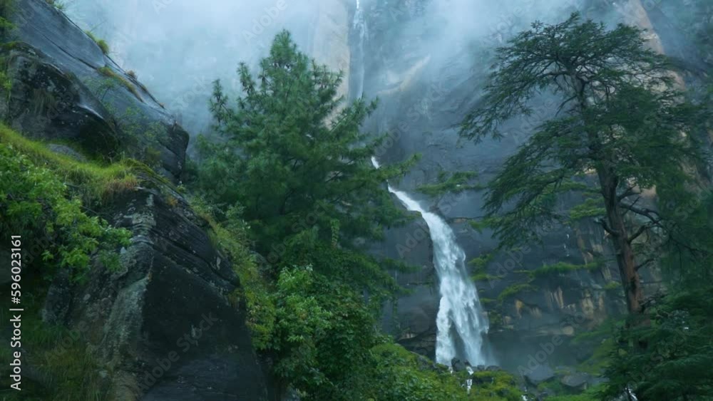 Slow motion shot of flowing Jogini waterfall covered with lush green trees in mountains of Manali, Himachal Pradesh, India. Tranquil View of Jogini falls with rain and foggy weather during monsoon. 