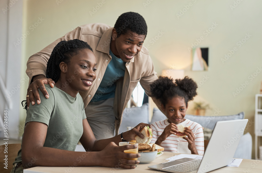 Family of three having a video call on laptop while sitting at table and having lunch