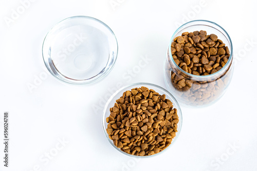 Dry pet food in a glass jar, bowl and water close-up on a white background. View from above