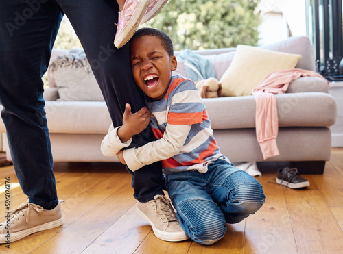 Hes having a bad day. a little boy throwing a tantrum while holding his parents leg at home.