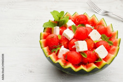 Watermelon Feta salad with watermelon scoops,feta cheeses and mint leaves in watermelon basket with white wood table background.Fresh and healthy Italian summer salad.Copy space