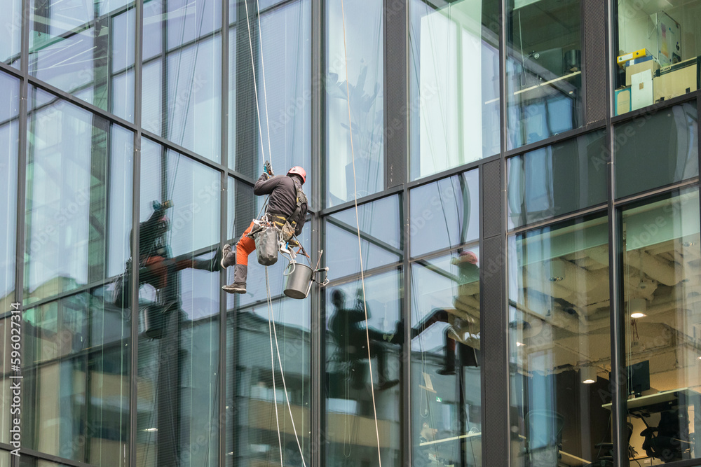 One window cleaners hanging on ropes on a skyscraper in Warsaw, Poland. reflection, glass, windows.