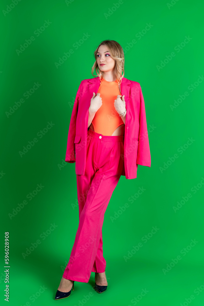 Young curly blonde dressed in pink blazer and pants, posing against a green screen. Isolated on green background. Young curly blonde dressed in pink blazer and pants, posing against a green screen. Isolated on green background.