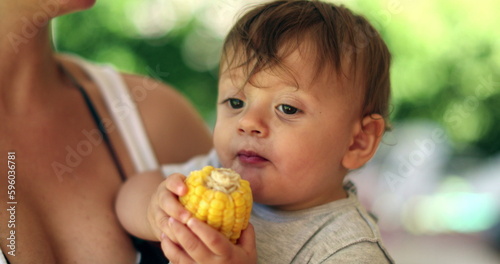 Adorable baby toddler holding corn cob offering to mother