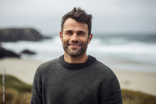 Portrait of handsome man smiling at camera while standing on the beach © Robert MEYNER