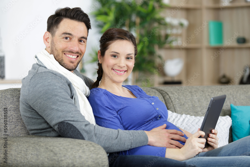 expectant couple sat on sofa looking at tablet pc expectant couple sat on sofa looking at tablet pc