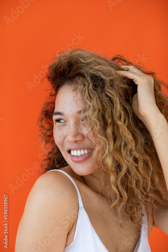 Smiling woman with curly hair and freckles on her face on orange background.