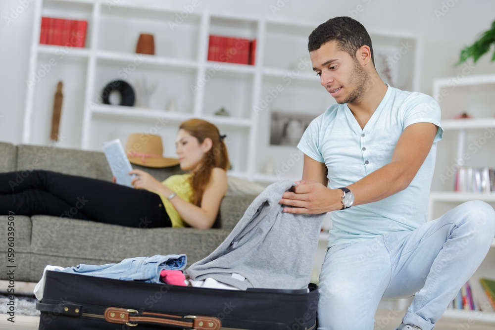 Fototapeta premium man packing suitcase while lady reads on the sofa