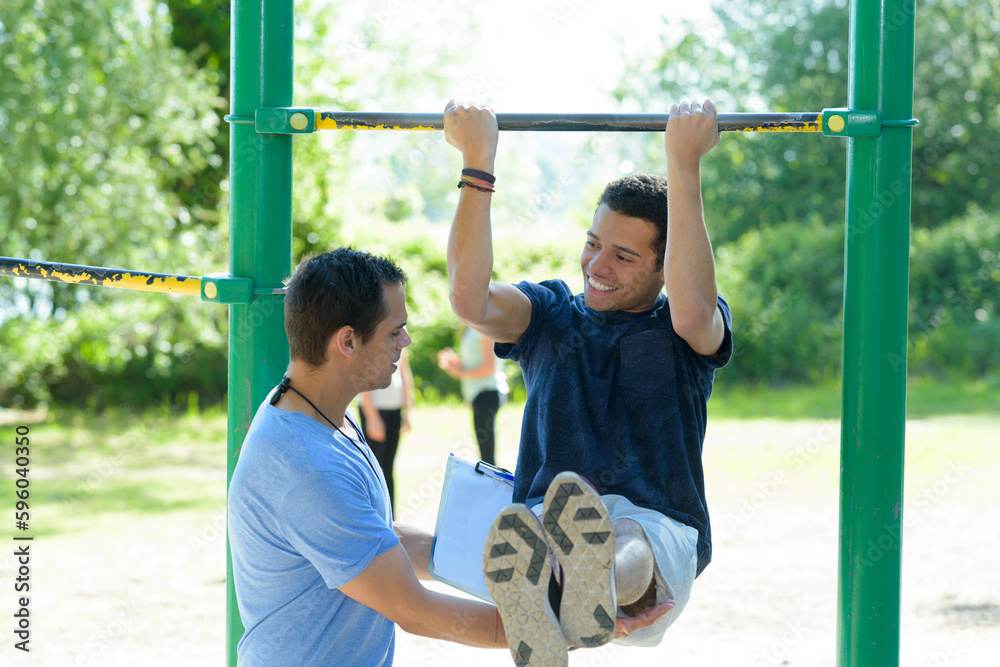 Naklejka premium young man with trainer doing leg raises outdoors