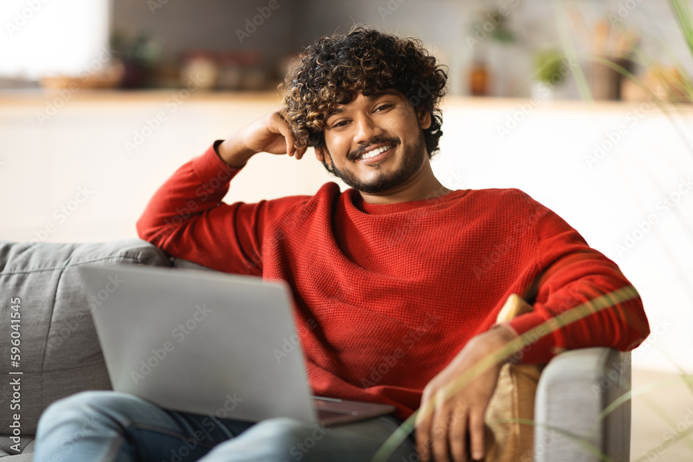 Portrait Of Smiling Indian Man With Laptop Sitting On Couch At Home Portrait Of Smiling Indian Man With Laptop Sitting On Couch At Home