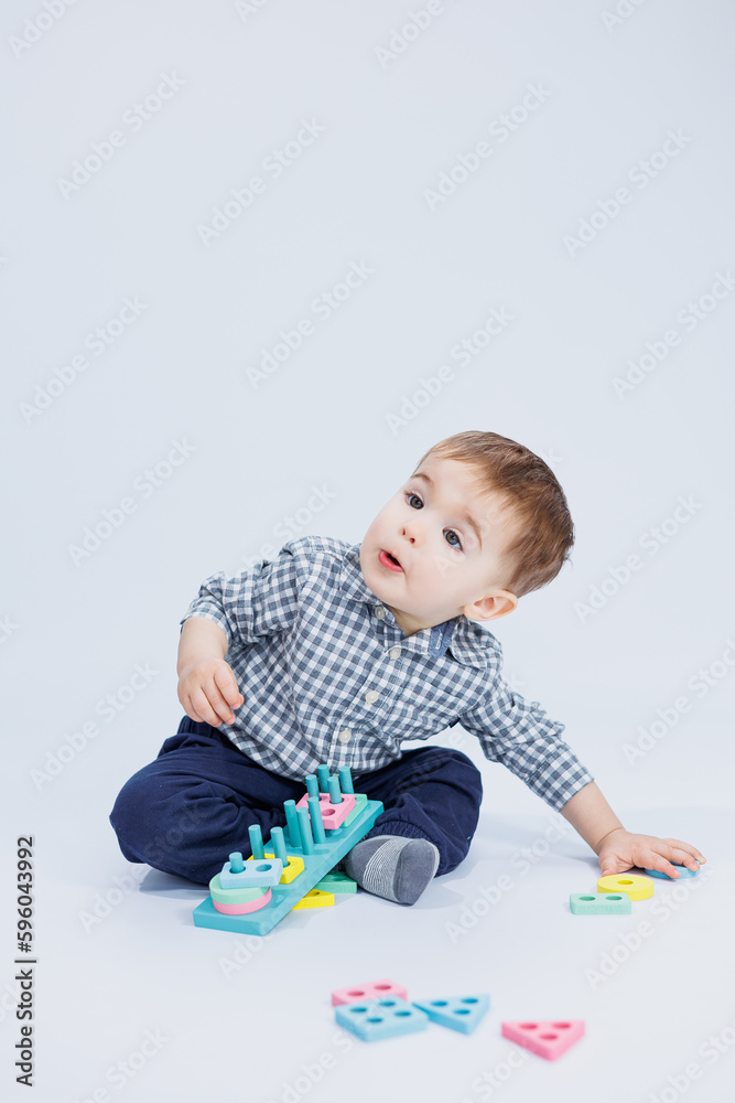 A cute little boy in a checkered shirt sits on a white background and plays with wooden educational toys. Ecological wooden toys for children A cute little boy in a checkered shirt sits on a white background and plays with wooden educational toys. Ecological wooden toys for children