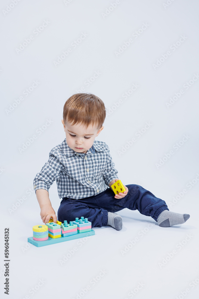 A little boy in a shirt is building a colorful wooden toy on a white background. The concept of children's development, games for children, toys. Copy space A little boy in a shirt is building a colorful wooden toy on a white background. The concept of children's development, games for children, toys. Copy space
