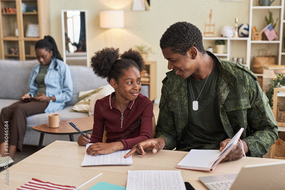 Military dad helping his daughter with her homework while they sitting at table in the living room Military dad helping his daughter with her homework while they sitting at table in the living room