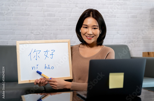 Young Asian female teacher teaching a chinese language via online distance teaching method on laptop at home. Chinese native speaker tutoring linguistics class on internet. photo