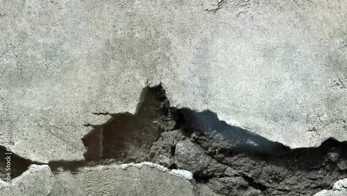 Concrete wall with a large hole knocked out. Looped 4K stock footage of the damaged surface.