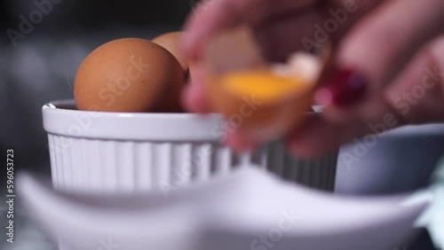 Slow de ovos vermelhos dentro de ramequim e mão com ovo quebrado com gema dentro caindo no prato  photo