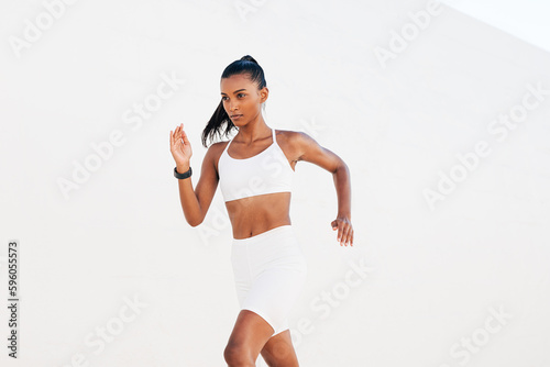 Fototapeta Naklejka Na Ścianę i Meble -  Slim female sprinter exercising outdoors at white wall. Young slim woman jogging at a day in white sportswear.