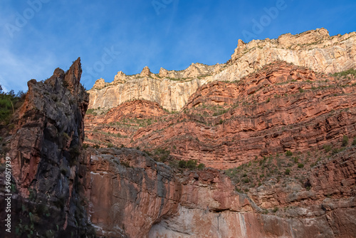 Scenic view on a massiv cliff seen from Bright Angel hiking trail at South Rim of Grand Canyon National Park, Arizona, USA. Light shining on steep stone wall and rock formations with blue sky