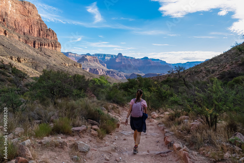 Rear view of woman with backpack hiking along Bright Angel trail with panoramic aerial overlook of South Rim of Grand Canyon National Park, Arizona, USA, America. Amazing vista after sunrise in summer © Chris