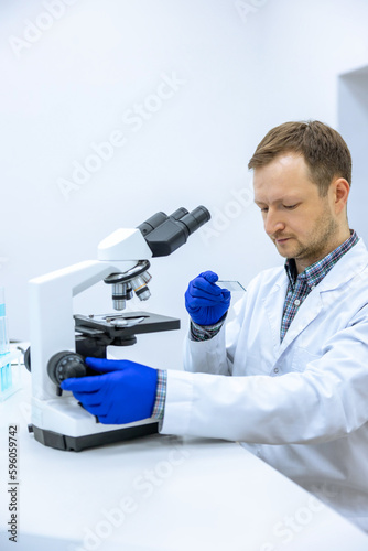 Scientist man doing chemical experiment, making analyzing, looking at sample on glass at laboratory