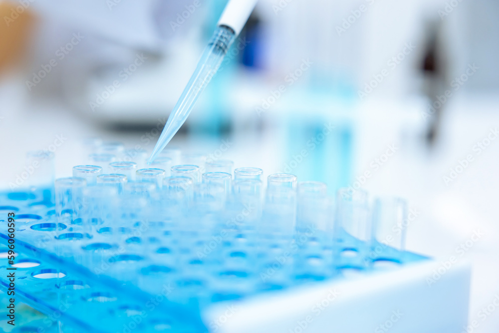 Unrecognizable scientist dripping blue liquid from pipette into test tube at table in laboratory.