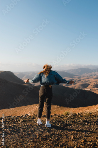 young woman feeling free with long hair in the wind and urban outfit enjoying the sunset on a desert hill in fuerteventura