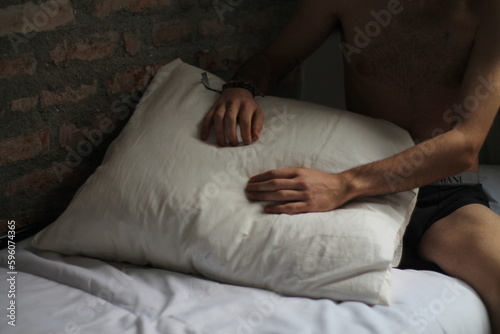 Relaxation and Inner Peace: Naked Men with his hands Holding a Pillow in White Bed Against Brick Wall, Inspiring the Mind to Meditate and Unwind