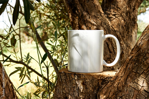 White coffee mug mockup on tree trunk wood through olives tree. Empty mug mock up for design promotion