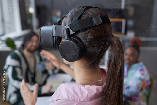Rear view of young woman testing VR glasses together with her colleagues during teamwork at meeting