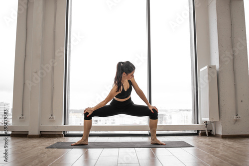 Fototapeta Caucasian woman squatting with feet shoulder width apart, holding hands on hips and twisting torso into sides