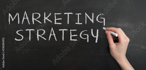 A woman's hand write text MARKETING STRATEGY with chalk on chalkboard