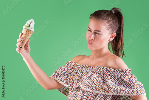 The girl carefully looks at the ice cream in the cone. On a green girl eats ice cream isolated background. The girl eats the taste of ice cream summer sundress on a girl who eats ice cream